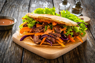 Pita - big sandwich with pulled beef and fresh vegetables on wooden table
