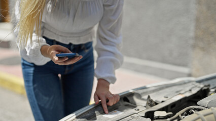 Young blonde woman texting to insurance for car breakdown at street