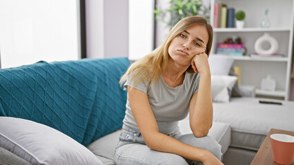 Attractive young blonde woman sitting with a serious expression, contemplating her problems on a...