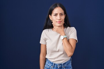 Young hispanic woman standing over blue background touching painful neck, sore throat for flu, clod...
