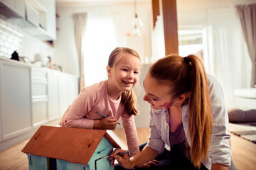 Mother and daughter enjoying crafting a dollhouse together at home