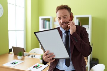 Naklejka premium Middle age man business worker talking on smartphone reading document at office