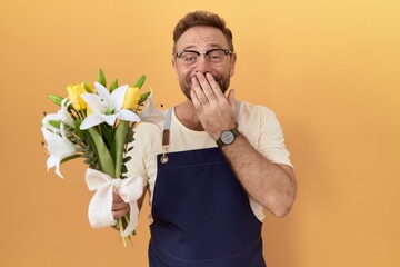 Middle age man with beard florist shop holding flowers laughing and embarrassed giggle covering...