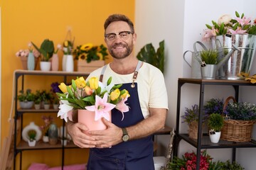Middle age man with beard working at florist shop holding plant looking positive and happy standing and smiling with a confident smile showing teeth