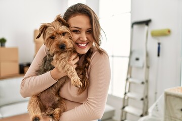 Young beautiful hispanic woman smiling confident hugging dog at new home