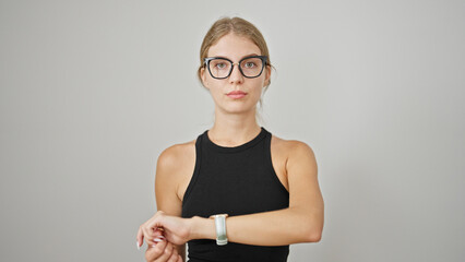 Young blonde woman standing with serious expression looking watch over isolated white background