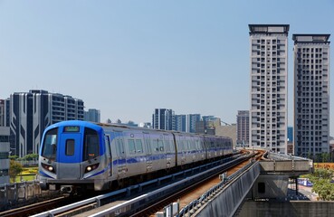 A metro train travels on the elevated rails of Taoyuan Airport MRT System with residential tower...