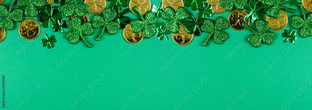 Poster St Patricks Day top border of  shiny shamrocks and gold coins. Top view over a green banner background with copy space.