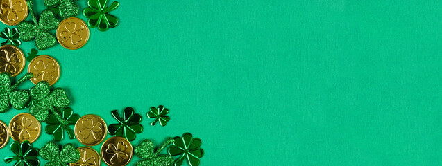 St Patricks Day corner border of  shiny shamrocks and gold coins. Top view over a green banner...