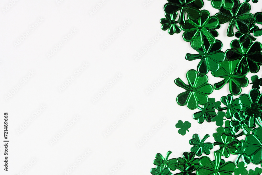 Poster St Patricks Day side border of  shiny shamrocks. Overhead view over a white background with copy space.