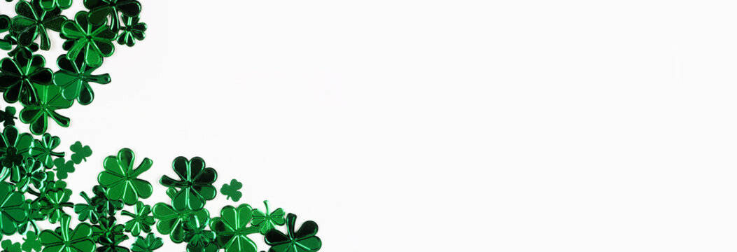 St Patricks Day corner border of  shiny shamrocks. Top down view over a white banner background with copy space.