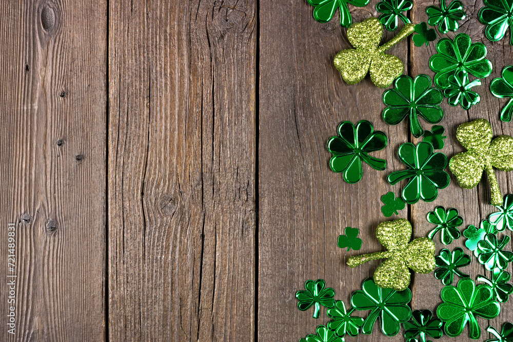 Poster St Patricks Day side border of  shiny shamrocks. Overhead view over a rustic dark wood background with copy space.