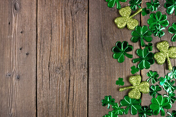 St Patricks Day side border of  shiny shamrocks. Overhead view over a rustic dark wood background with copy space.