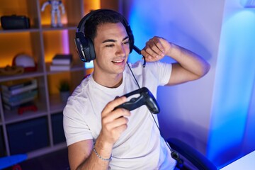 Young hispanic man streamer playing video game using joystick at gaming room