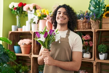 Young latin man florist holding bouquet of flowers at flower shop