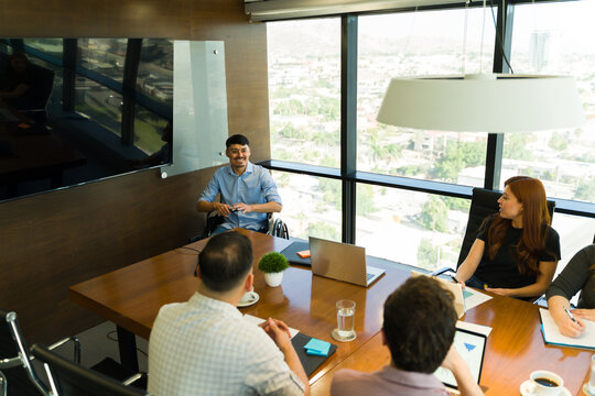 Happy Latin man in a wheelchair leading a team meeting with some of his employees