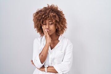 Young hispanic woman with curly hair standing over white background thinking looking tired and bored with depression problems with crossed arms. - obrazy, fototapety, plakaty