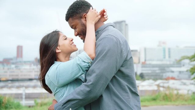 A handsome man and beautiful woman hugging each other in the park with a modern city in the background	