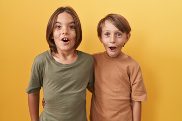 Adorable boys hugging in astonishment, open-mouthed disbelief reaction expressing funny fear and wonder, standing against yellow isolated background - obrazy, fototapety, plakaty