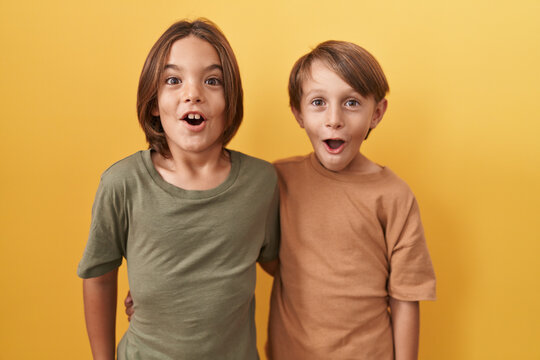 Adorable boys hugging in astonishment, open-mouthed disbelief reaction expressing funny fear and wonder, standing against yellow isolated background