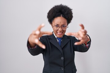 Beautiful african woman with curly hair wearing business jacket and glasses shouting frustrated with rage, hands trying to strangle, yelling mad