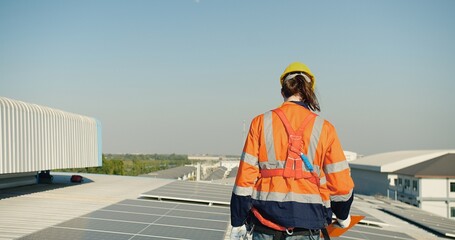Solar engineer in reflective safety vest and helmet oversees a rooftop solar panel array...