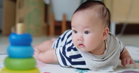 adorable baby lies on floor, gazing curiously at vibrant stacking rings, capturing a moment of early childhood development, Infant focused on colorful stacking rings while practicing crawling