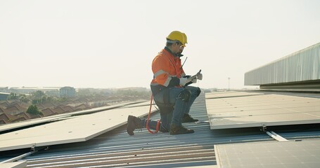 Two technicians in safety harnesses are working on the installation of solar panels on a sunny...