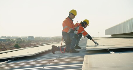 Two technicians in safety harnesses are working on the installation of solar panels on a sunny...