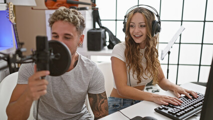 A woman and man sing in a recording studio, with a microphone, headphones, and music equipment...