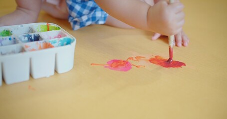 An engrossed toddler in a blue checkered dress discovers creativity with a paintbrush in hand and...