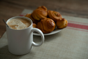 a cup of coffee and homemade buns on a plate.
