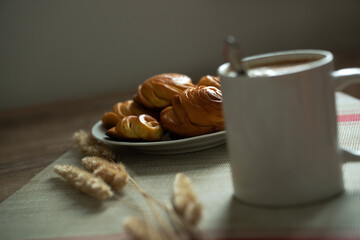 a cup of coffee and homemade buns on a plate, decorated with reed branches.