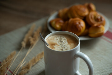 a cup of coffee and homemade buns on a plate, decorated with reed branches.