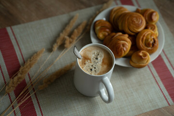 a cup of coffee and homemade buns on a plate, decorated with reed sprigs, serving napkin.