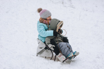 A little boy with a girl sister, happy children, a family ride while sitting on a sled, going down a hill in the snow in winter. Photography, portrait, childhood concept, lifestyle.