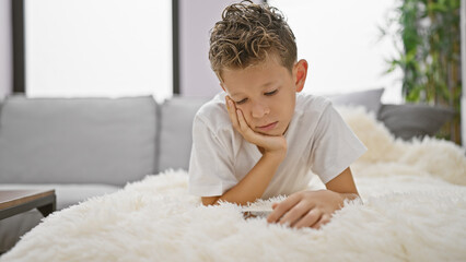 Fototapeta premium Blond boy using smartphone lying on sofa at home