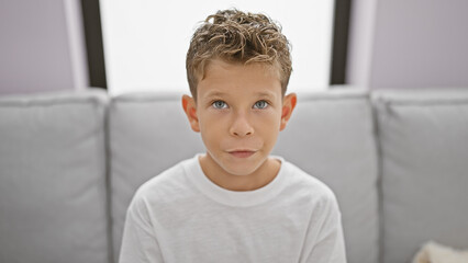 Adorable blond boy resting in a comfortable cozy living room, concentrating with a serious face...