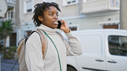 A young african american woman with dreadlocks talks on a phone while walking on an urban city...