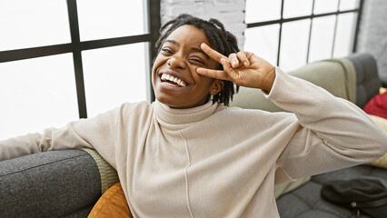 A joyful african american woman with dreadlocks posing playfully in a cozy living room setting.