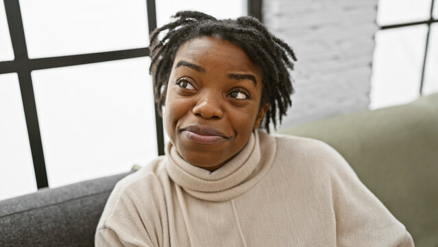 Young african american woman with dreadlocks sitting casually on a sofa indoors with a smiling expression.