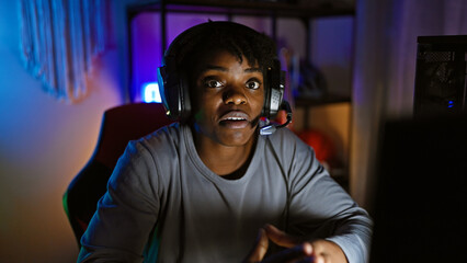 Focused african american woman with dreadlocks gaming at night in a dark room wearing a headset.