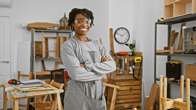 Confident young woman with dreadlocks wearing safety glasses in a carpentry workshop.