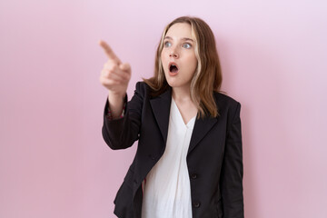 Young caucasian business woman wearing black jacket pointing with finger surprised ahead, open mouth amazed expression, something on the front