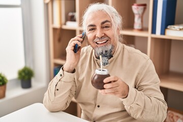 Middle age grey-haired man talking on smartphone drinking infusion at home