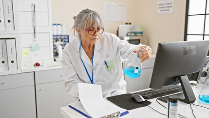 Mature woman scientist analyzing chemicals in a laboratory setting, with computer and lab equipment.