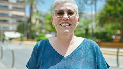 Middle age grey-haired woman wearing sunglasses smiling at street