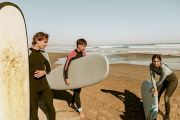 Surfers in wetsuits standing on beach with surfboards and preparing for ride on waves