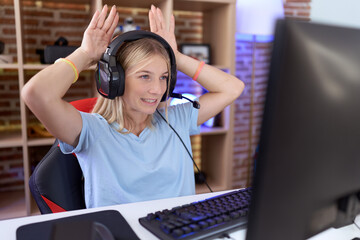 Young caucasian woman playing video games wearing headphones doing bunny ears gesture with hands...
