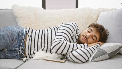 Handsome young arab man, with a relaxed beard, comfortably lying on his cozy living room sofa,...